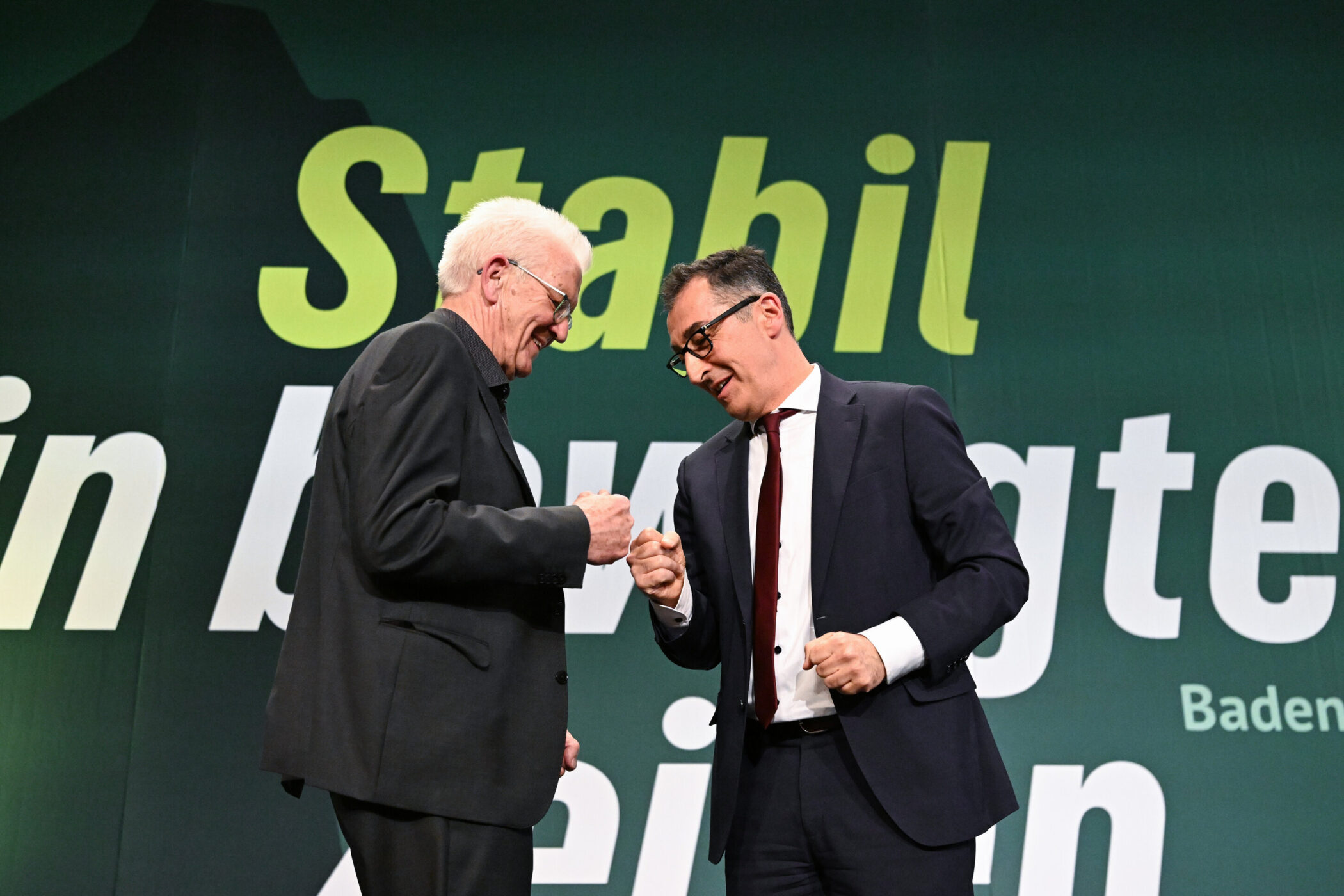 Zwei Männer geben sich auf einer Bühne die Faust, Hintergrund mit Text.