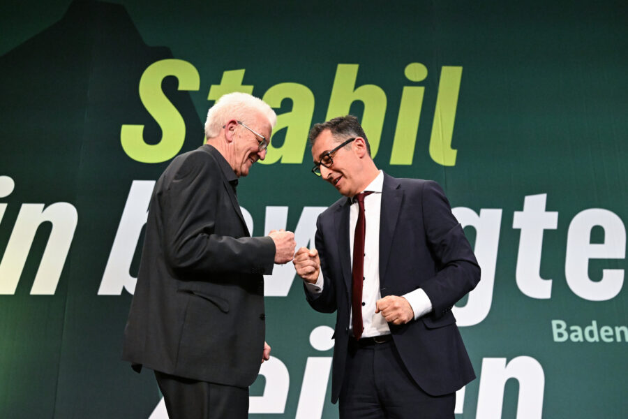 Zwei Männer geben sich auf einer Bühne die Faust, Hintergrund mit Text.