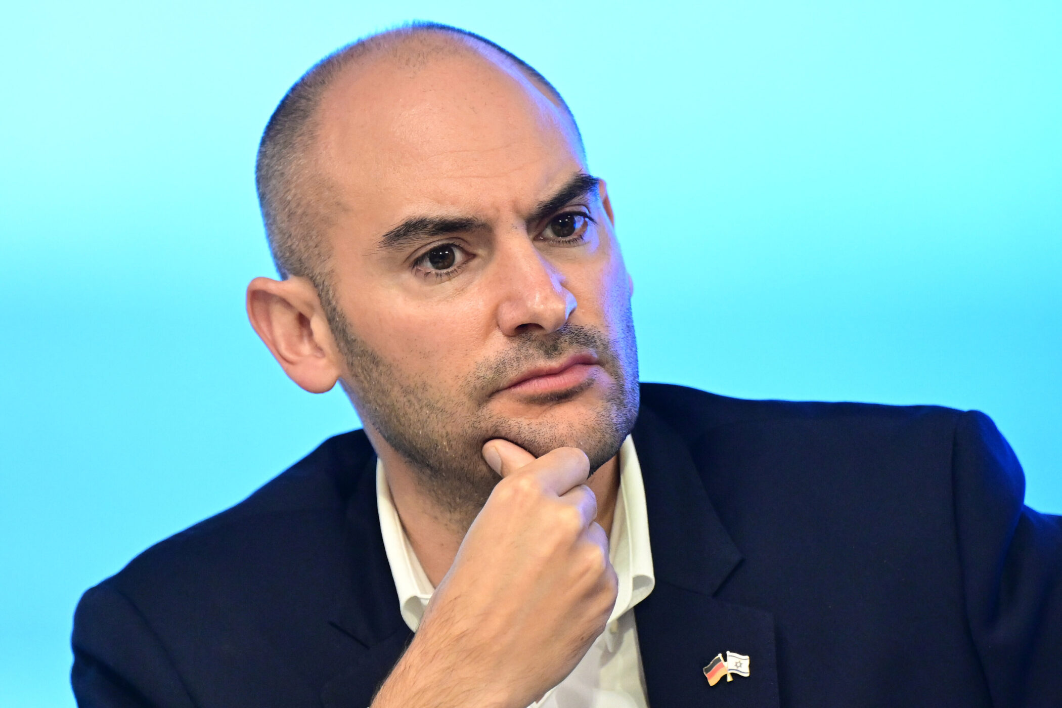 Ein Mann im Anzug stützt sein Kinn mit der Hand, blauer Hintergrund.