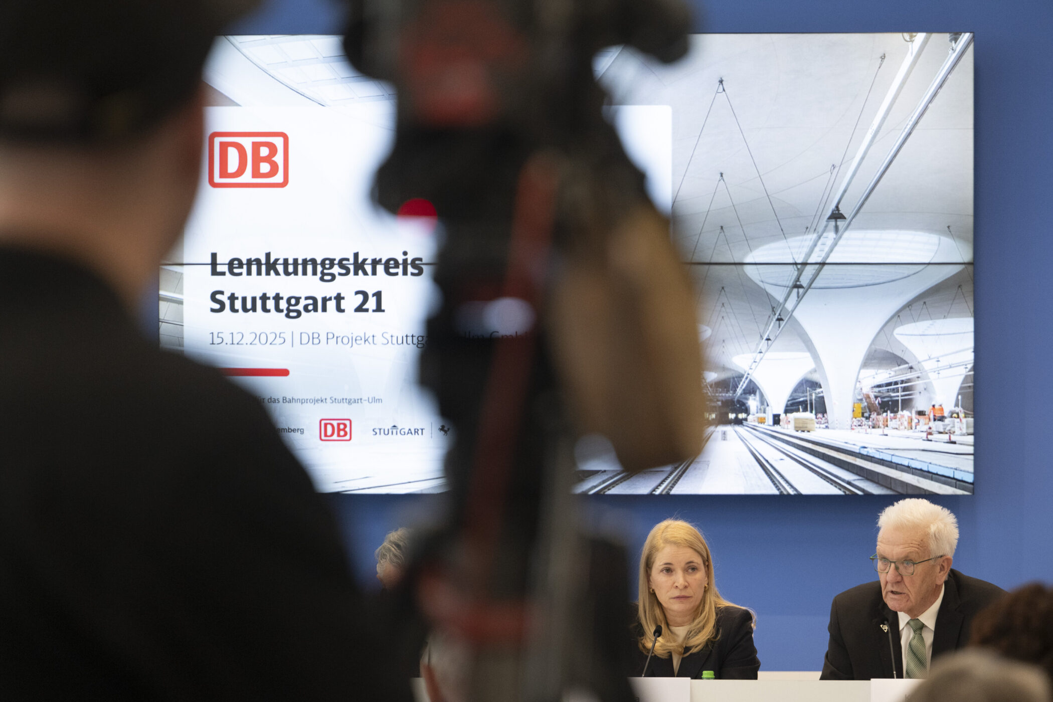 Zwei Personen bei einer Pressekonferenz, Bildschirm mit "Lenkungskreis Stuttgart 21".