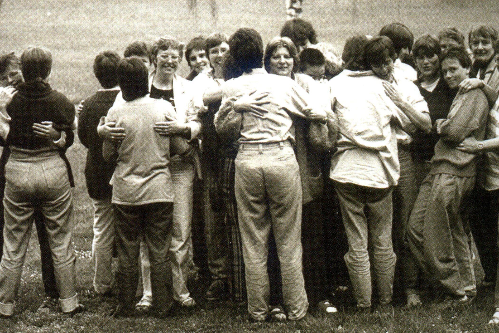 Gruppe von Menschen umarmt sich im Freien auf einer Wiese.