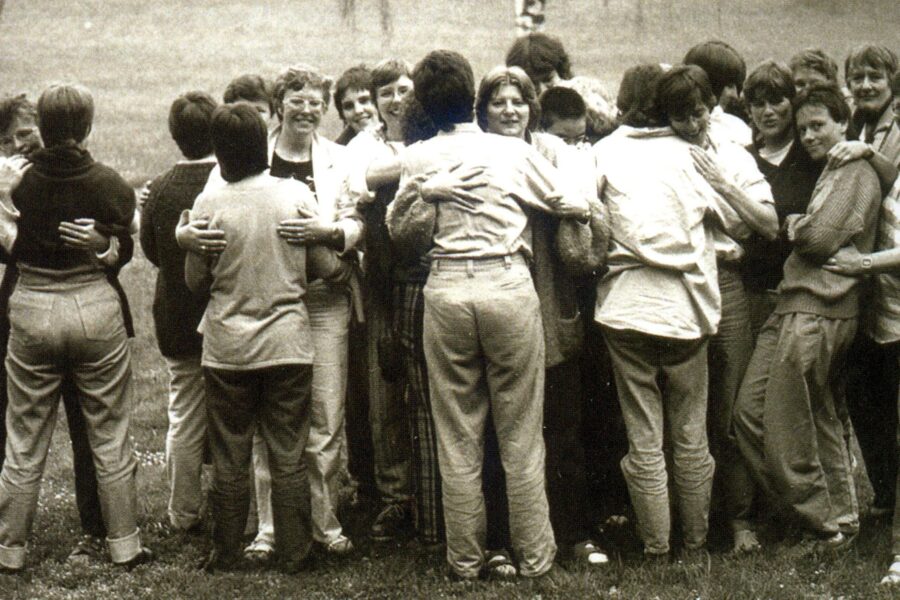 Gruppe von Menschen umarmt sich im Freien auf einer Wiese.