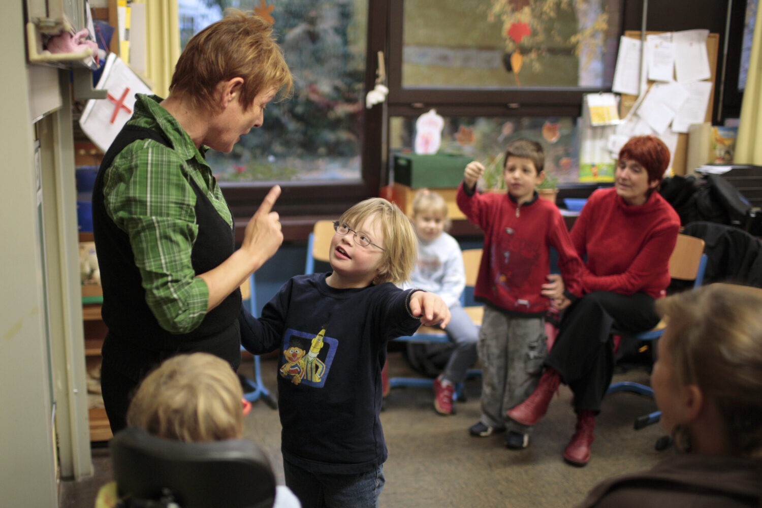 Fünf Personen in einem Raum, ein Kind zeigt auf eine Frau, die spricht.