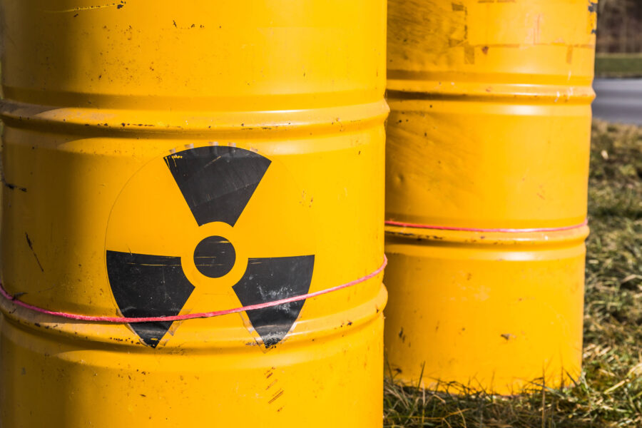 Gelbe Fässer mit schwarzem Warnsymbol für Radioaktivität, auf Gras stehend.