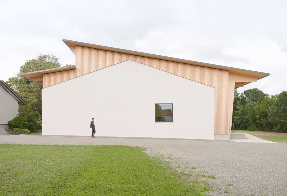 Person geht an modernem Gebäude mit schrägem Dach und kleinem Fenster vorbei.