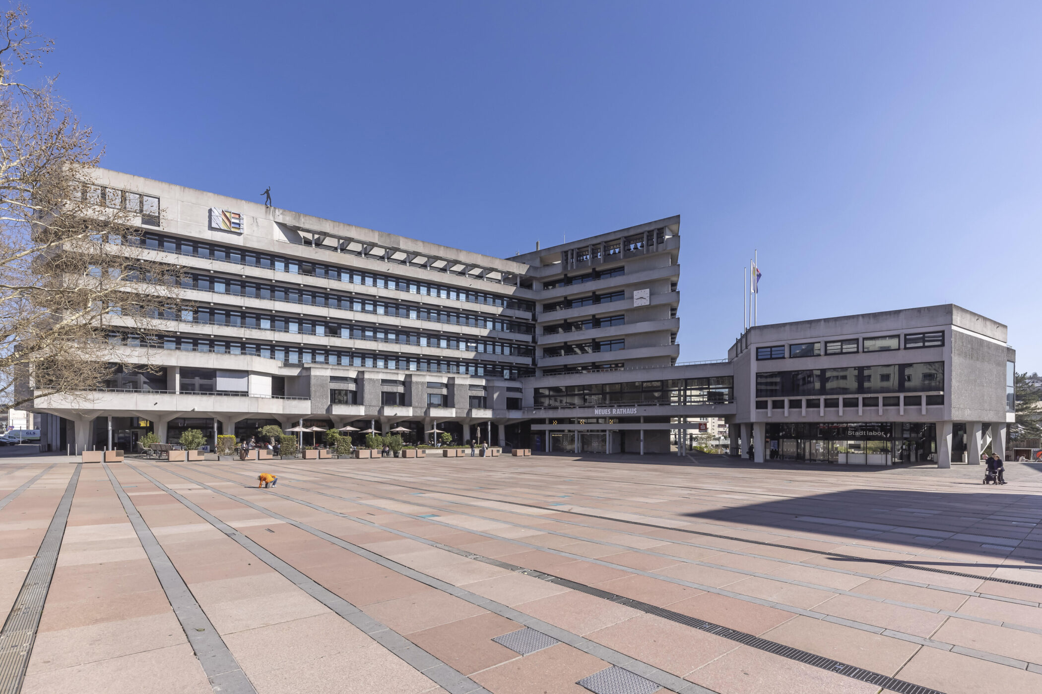Modernes Gebäude mit breiter Fassade, großer Platz davor, blauer Himmel.