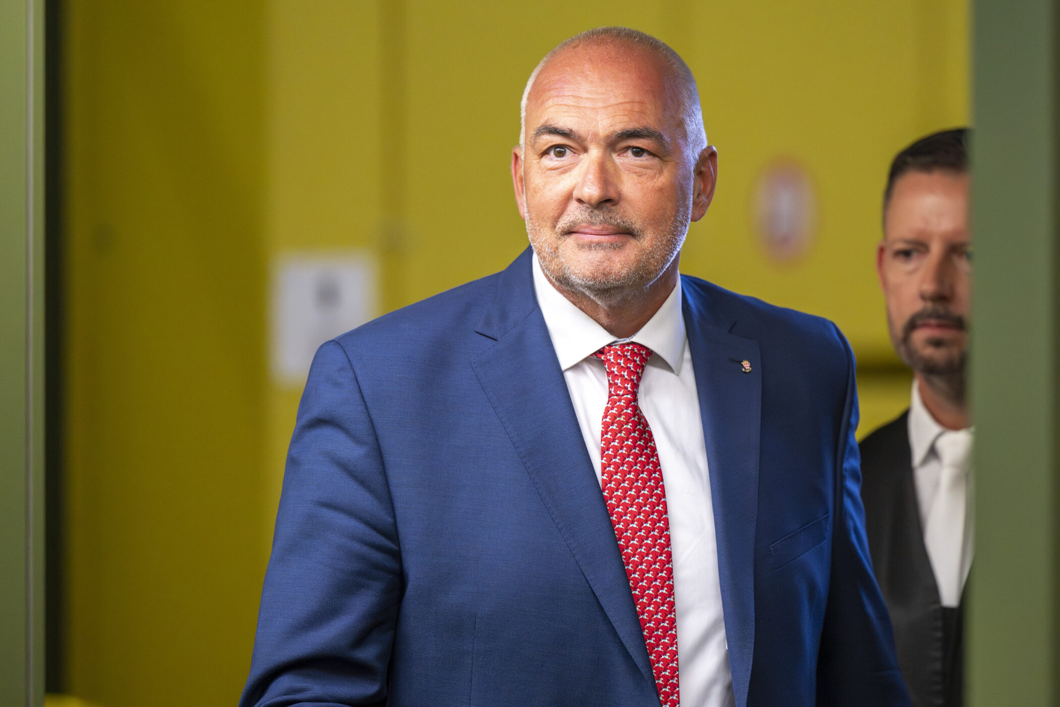 Zwei Männer in Anzügen betreten einen Raum mit gelber Wand.