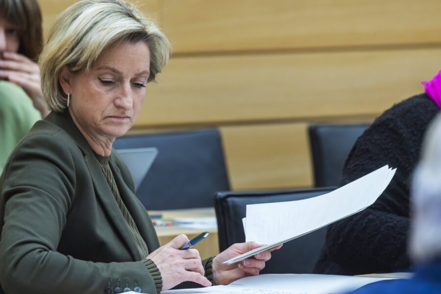 Eine Frau sitzt an einem Tisch und hält Papiere in der Hand.