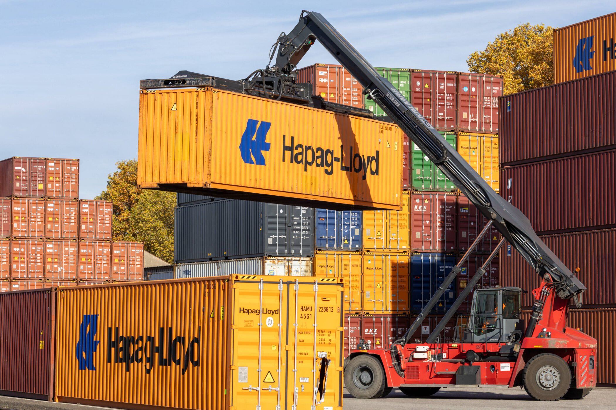 Ein roter Kran hebt einen gelben Container mit "Hapag-Lloyd"-Logo.