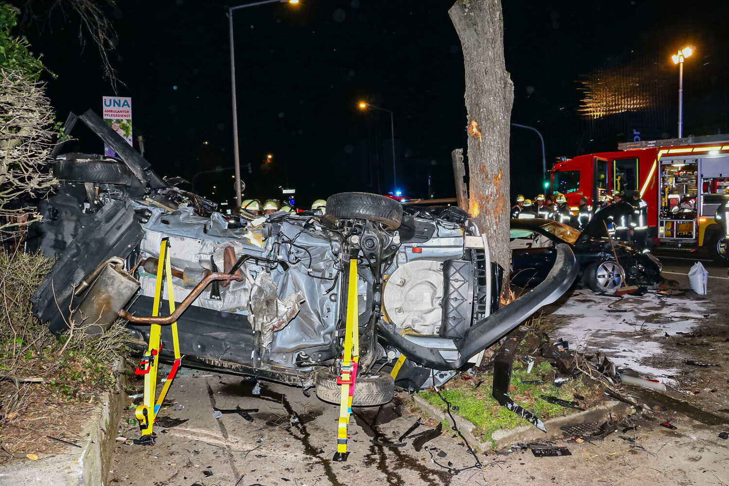 Verunfalltes Auto auf der Seite, Feuerwehrleute und Einsatzfahrzeug im Hintergrund.