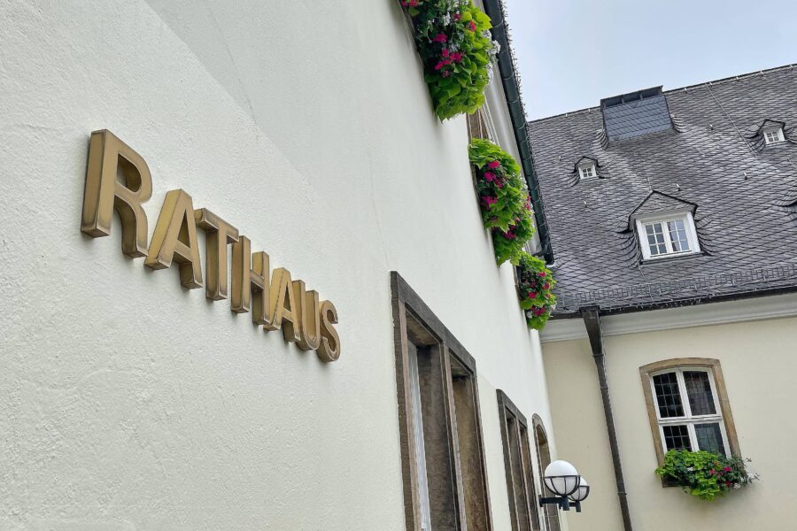 Rathaus-Schriftzug an weißer Wand, Fenster mit Blumenkästen, Schieferdach.