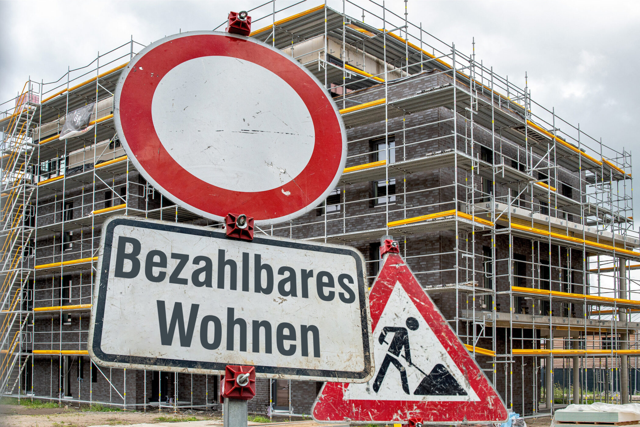 Verkehrsschilder vor einem eingerüsteten Gebäude, Text: "Bezahlbares Wohnen".