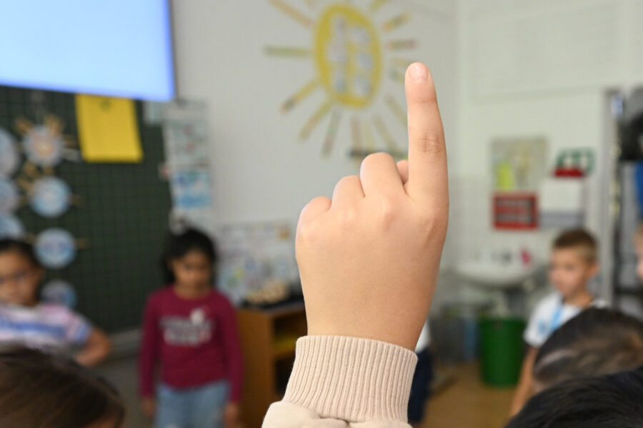 Hand eines Kindes zeigt nach oben, unscharfe Kinder im Hintergrund.
