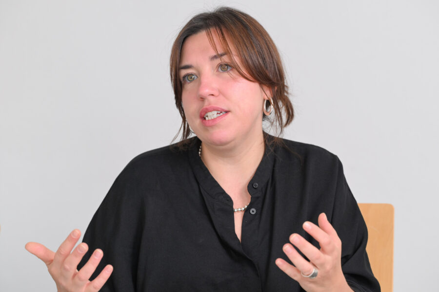 Frau mit dunklem Haar und schwarzer Bluse gestikuliert mit den Händen.