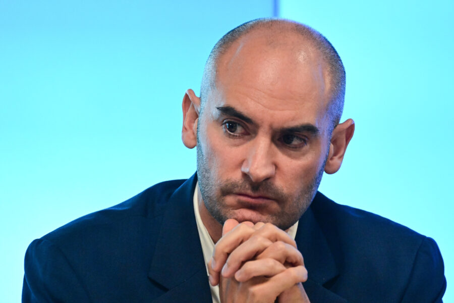 Ein Mann mit Glatze und Bart schaut nachdenklich, Hände gefaltet.