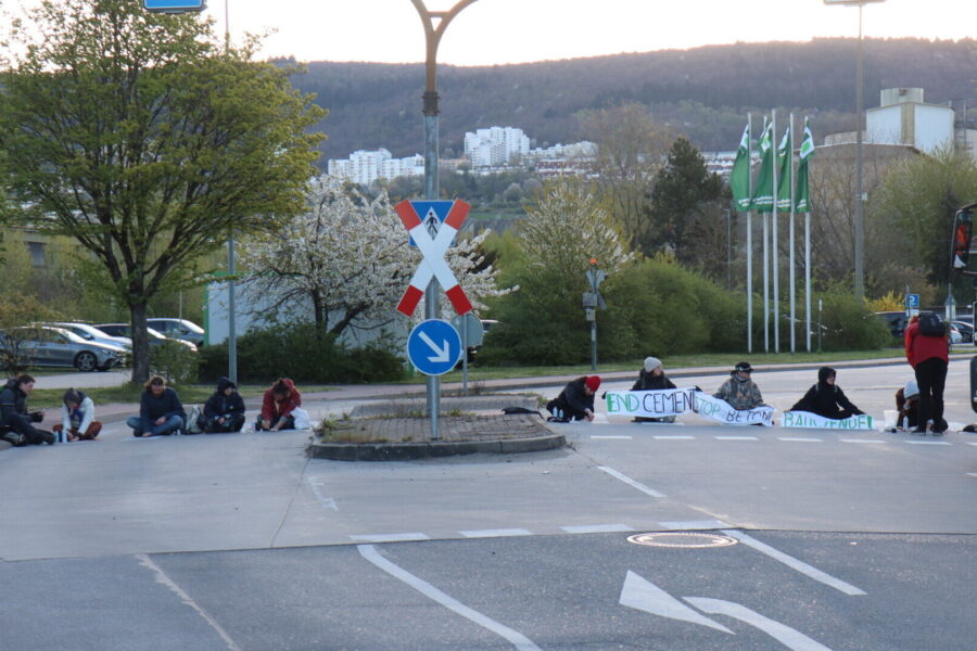 Mehrere Personen sitzen auf der Straße, halten ein Banner mit Text.