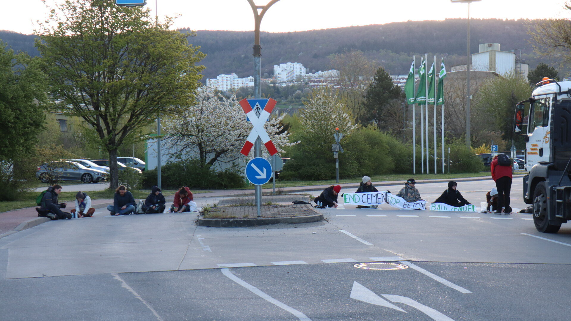 Mehrere Personen sitzen auf der Straße, halten ein Banner mit Text.