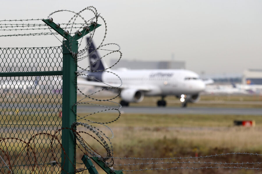 Stacheldrahtzaun im Vordergrund, unscharfes Flugzeug im Hintergrund auf Rollbahn.