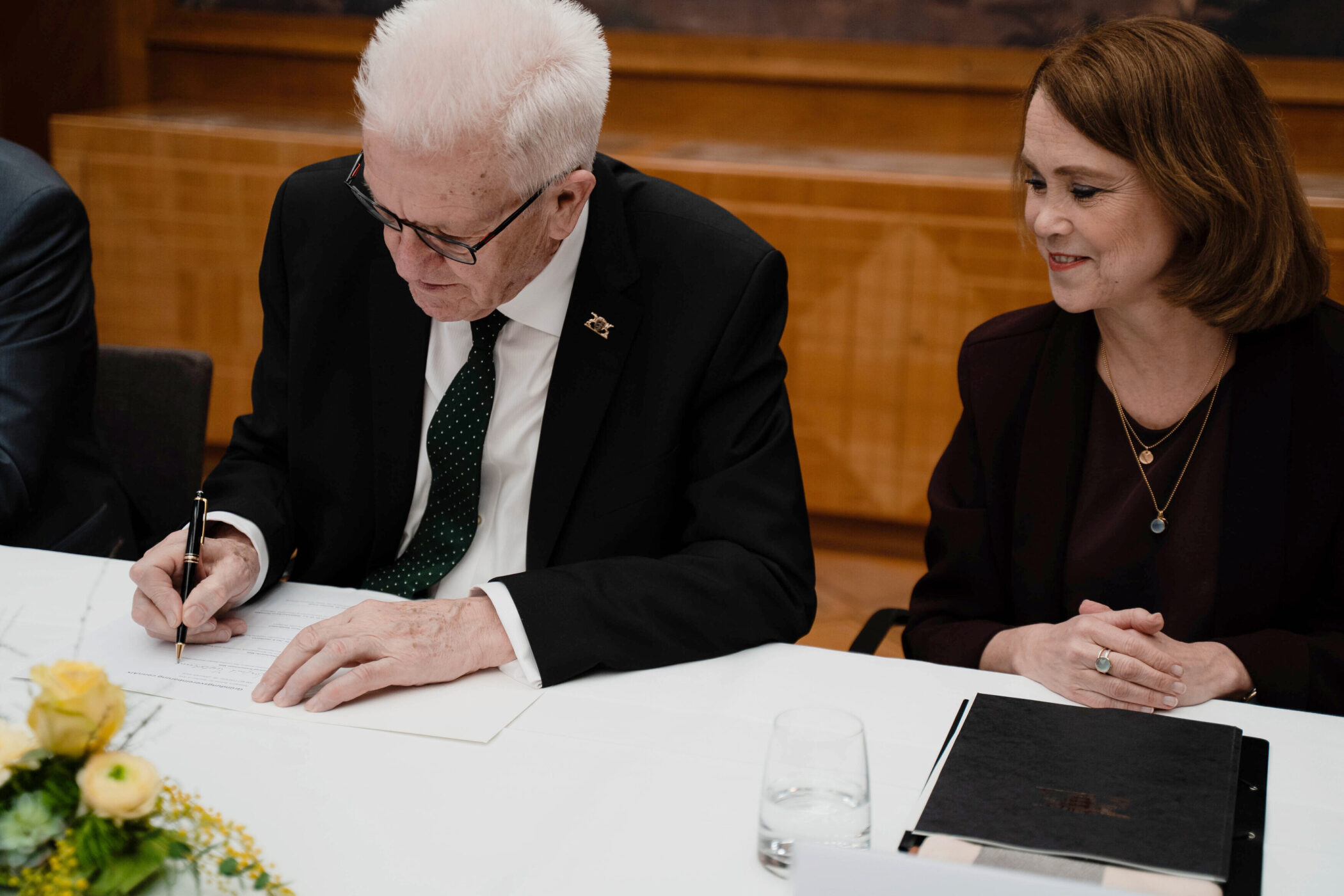 Zwei Personen an einem Tisch, eine Person unterschreibt ein Dokument.