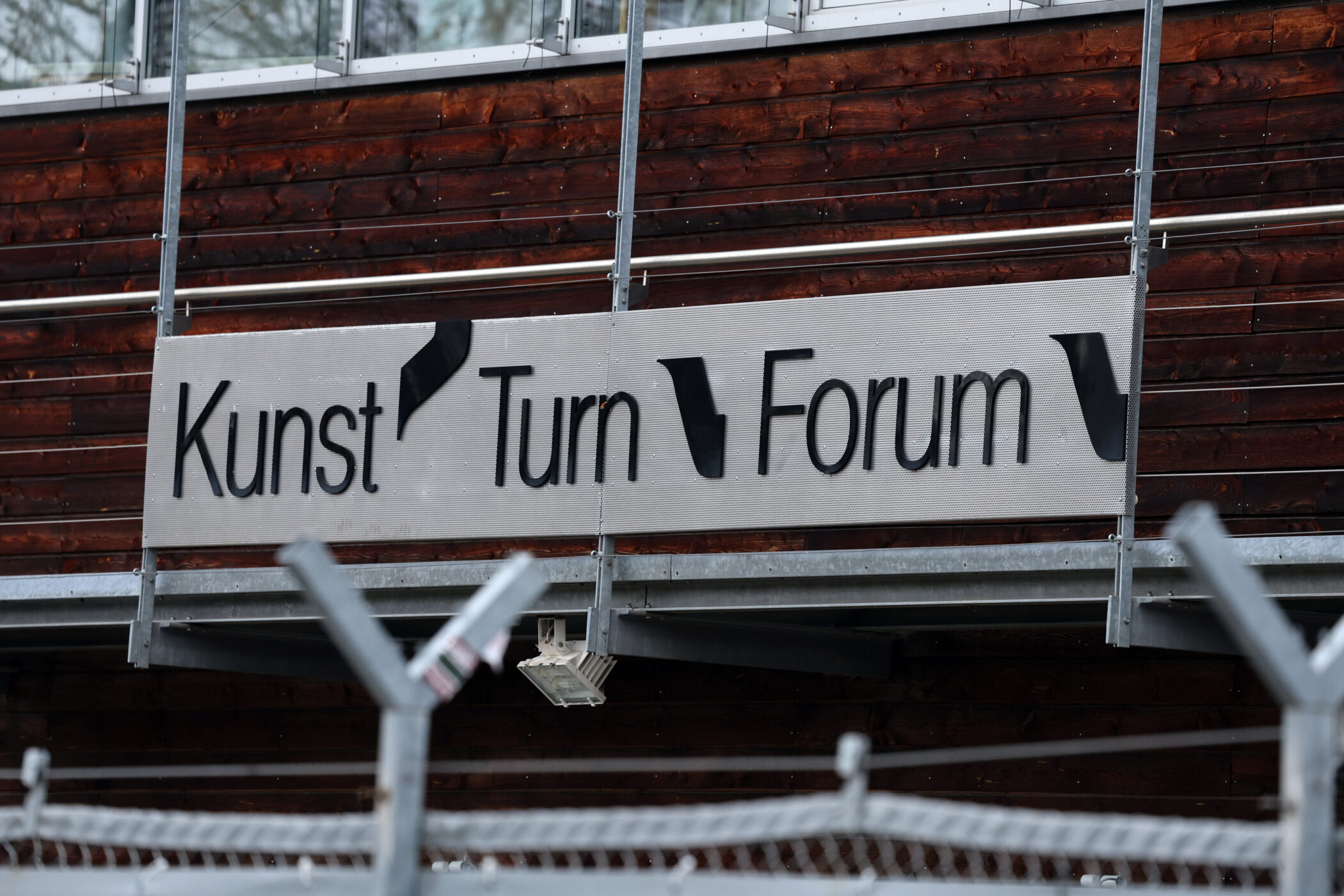 Schild mit Aufschrift "Kunst Turn Forum" an Holzwand, davor Zaun.