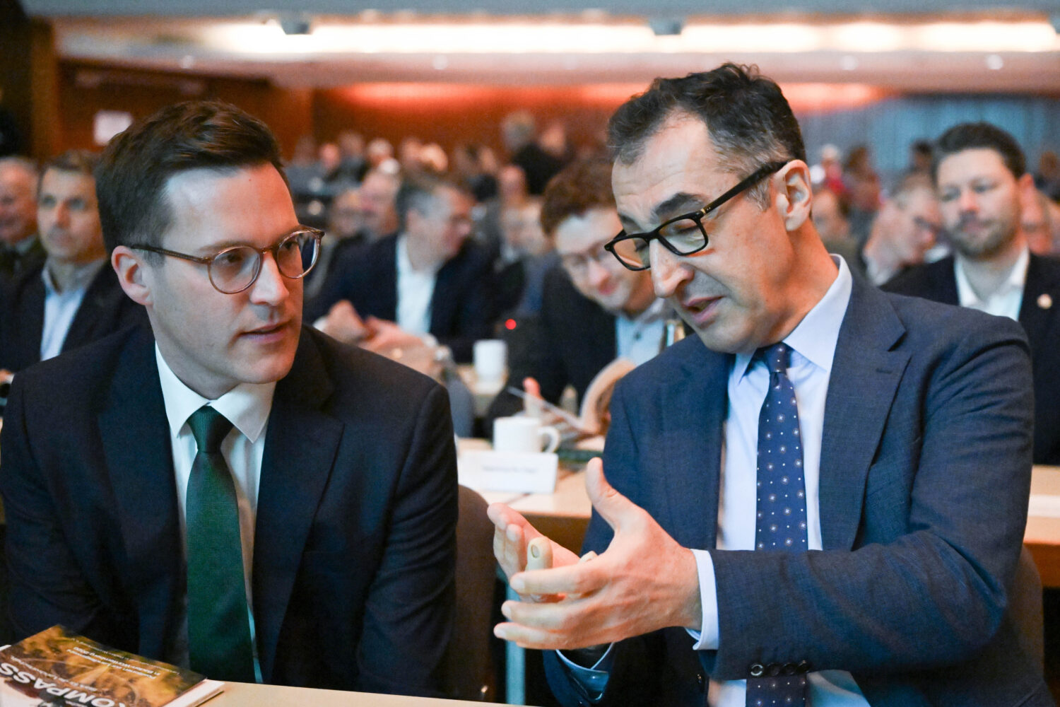 Zwei Männer in Anzügen unterhalten sich in einem Konferenzraum.