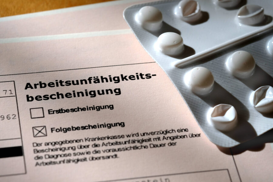 Arbeitsunfähigkeitsbescheinigung und Tablettenblister auf einem Tisch.