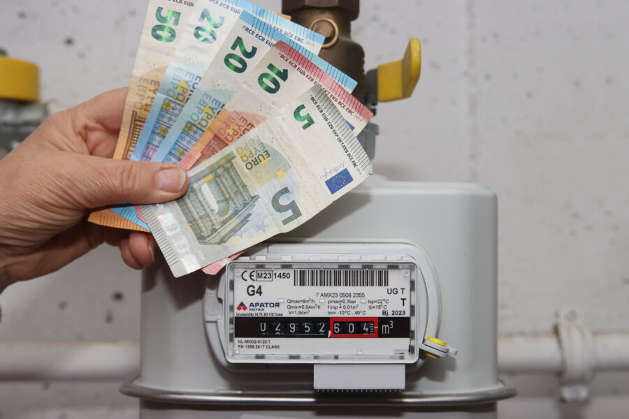 Hand hält Euro-Geldscheine vor einem Gaszähler mit sichtbarem Zählerstand.