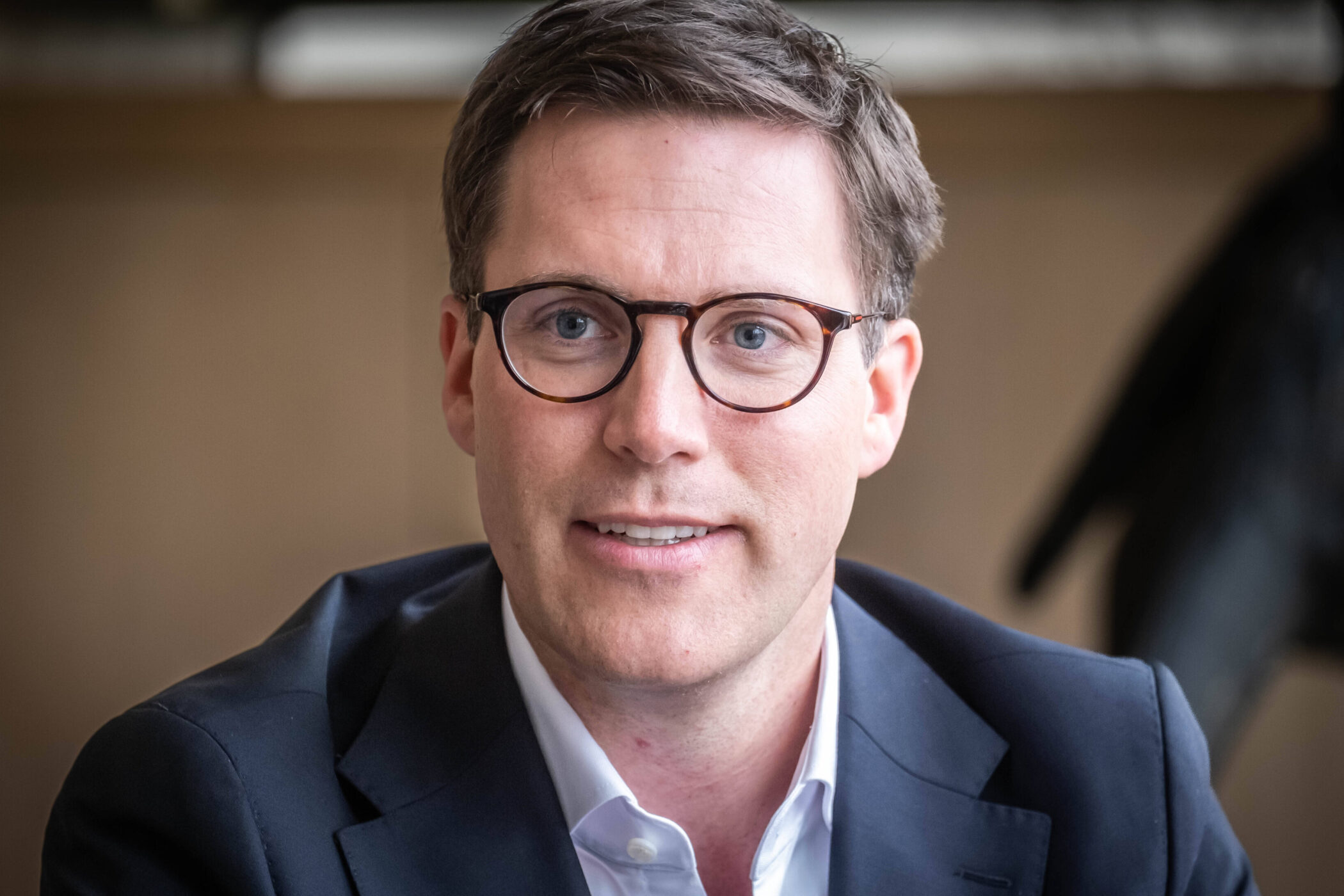 Ein Mann mit Brille und Anzug lächelt in die Kamera.