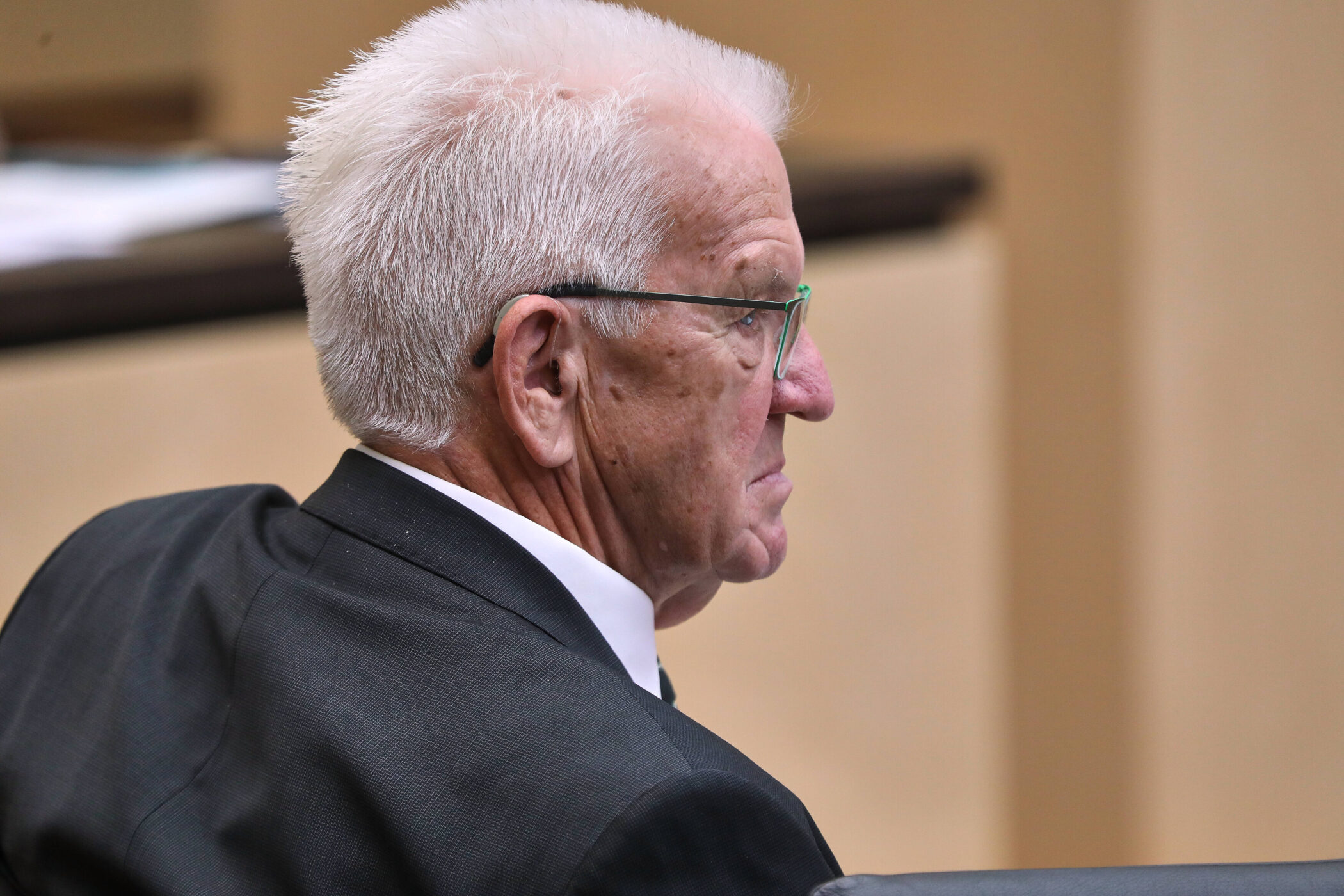 Älterer Mann mit Brille und weißem Haar in Anzug von der Seite.