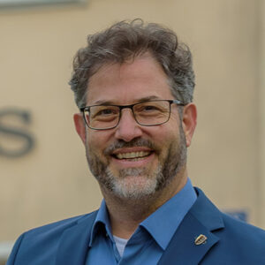 Ein Mann mit Brille und Bart lächelt in die Kamera.