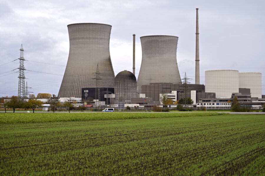 Kraftwerk mit Kühltürmen und Schornstein, davor grüne Wiese und Strommasten.