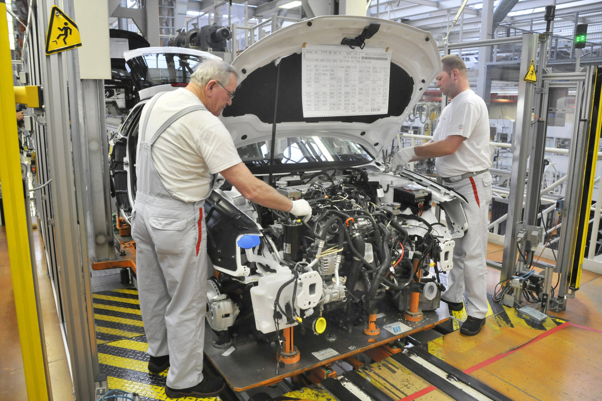 Zwei Männer arbeiten an einem Auto in einer Fabrikhalle.