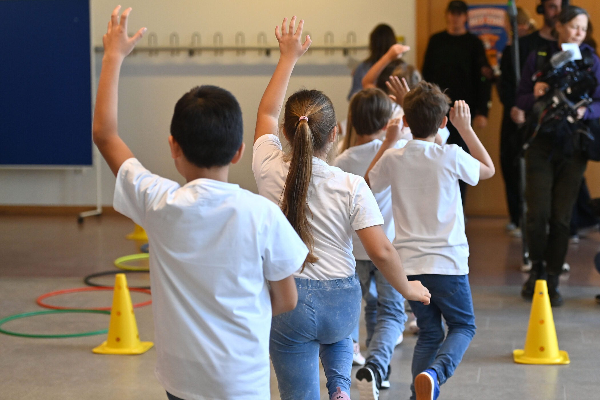Kinder in weißen T-Shirts laufen durch einen Raum, gelbe Hütchen am Boden.
