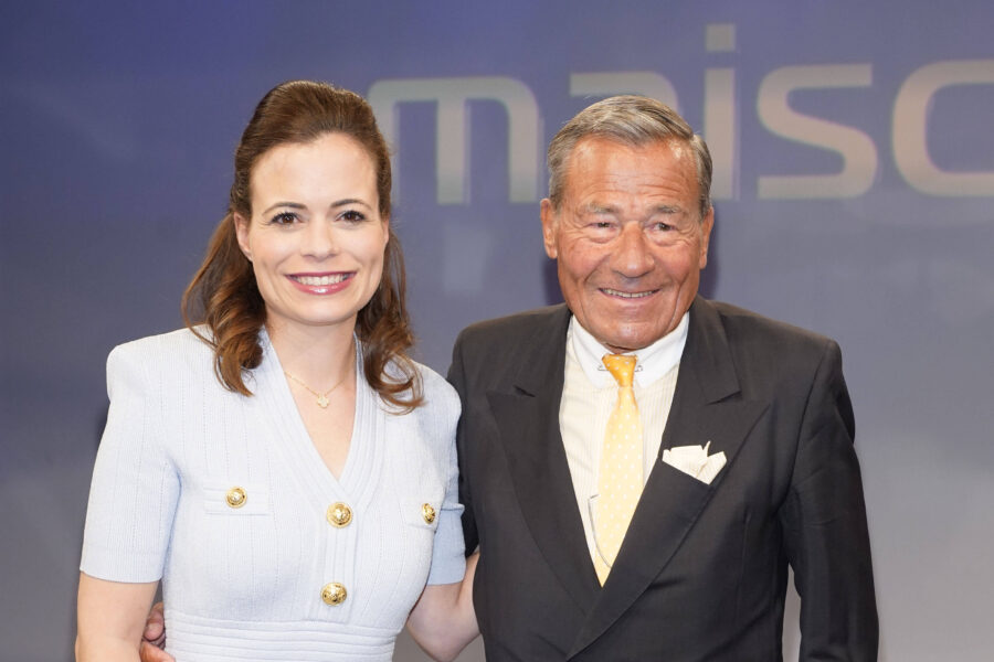 Zwei Personen lächeln in die Kamera, eine Frau und ein Mann in Anzügen.