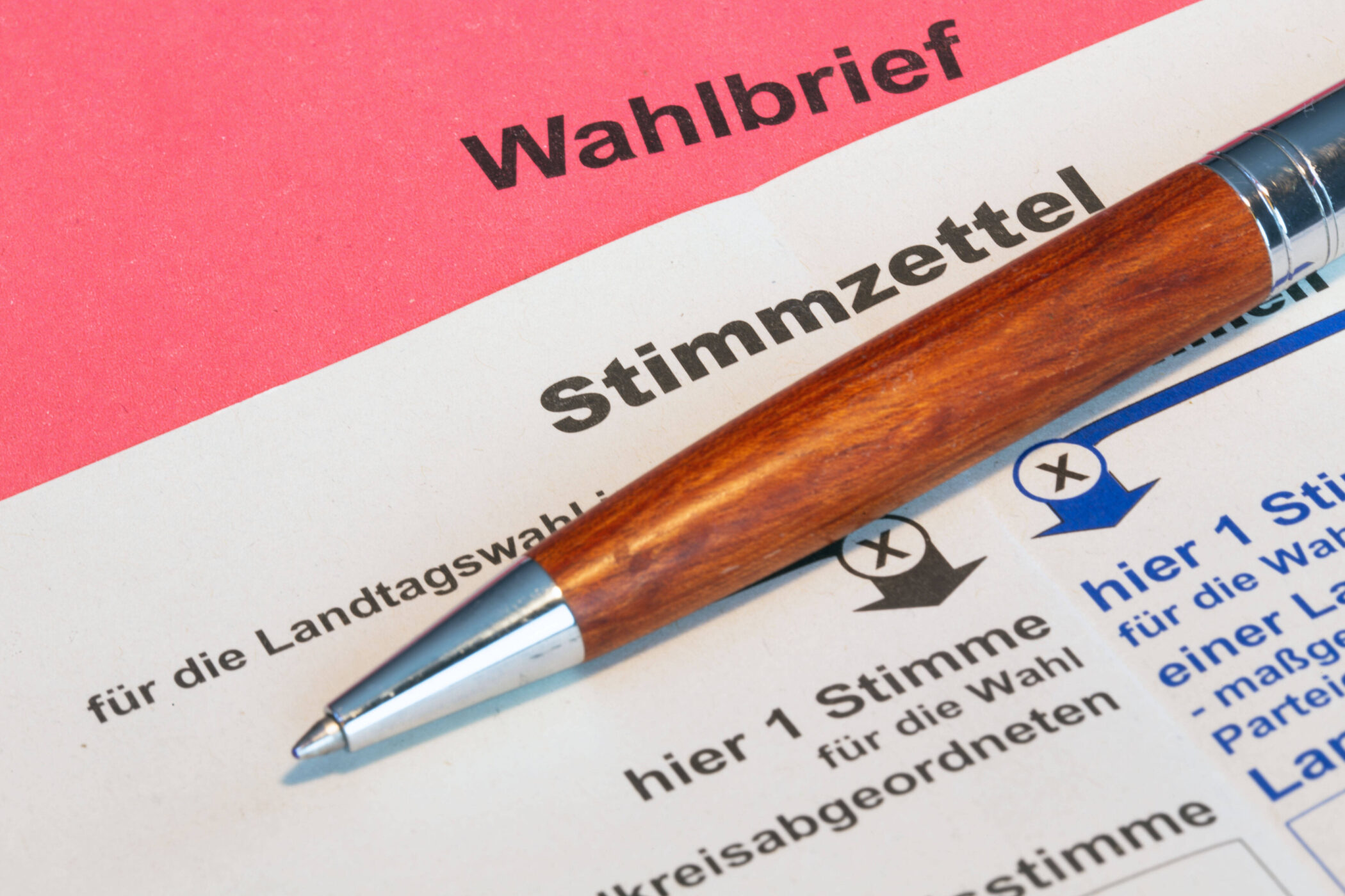 Roter Wahlbrief, Stimmzettel und Kugelschreiber.