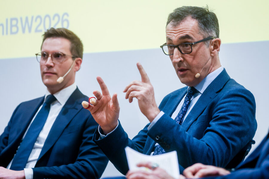 Zwei Männer in Anzügen mit Mikrofonen, einer spricht gestikulierend.