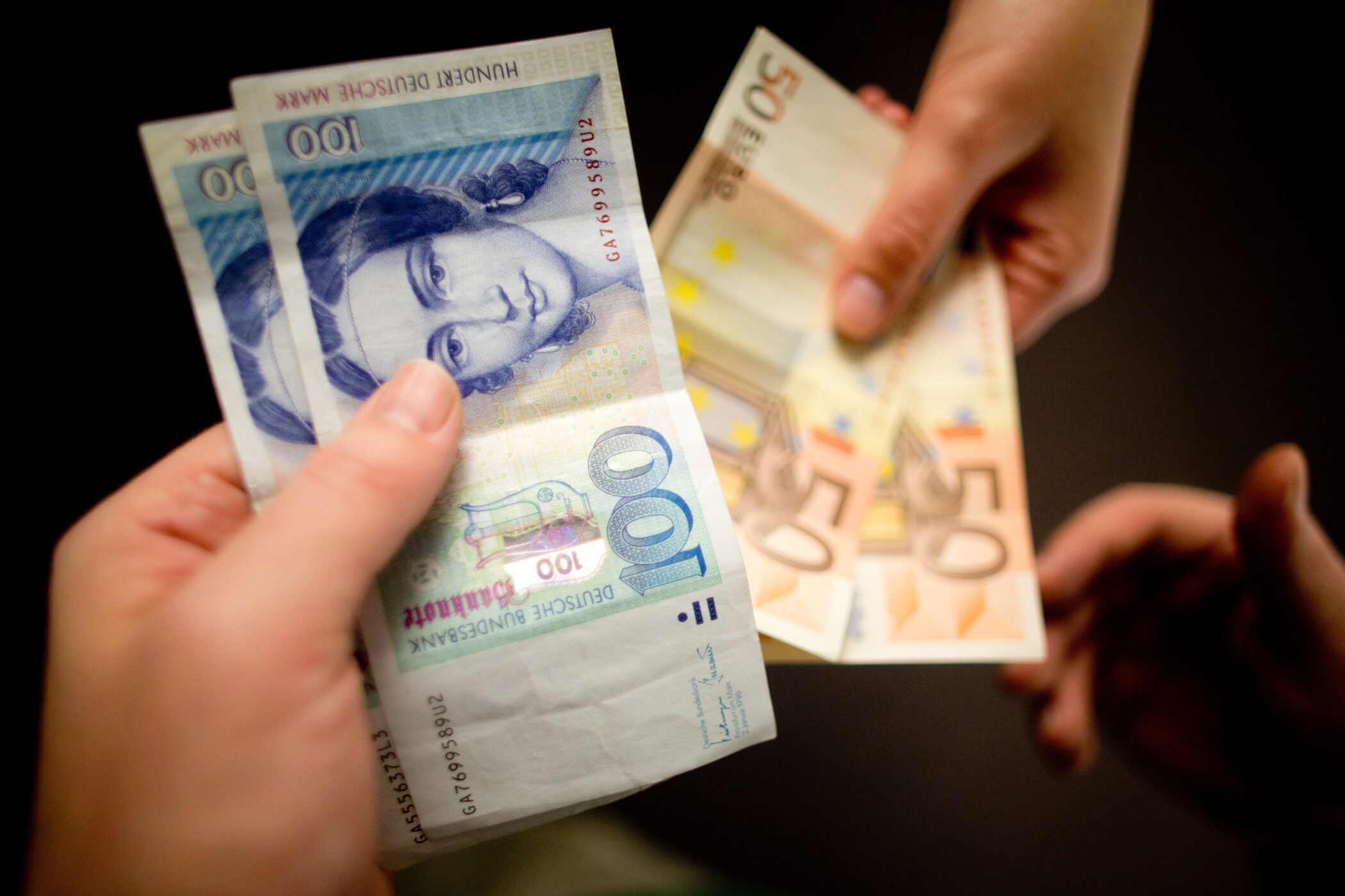 Zwei Hände tauschen 100-DM-Scheine gegen 50-Euro-Scheine.