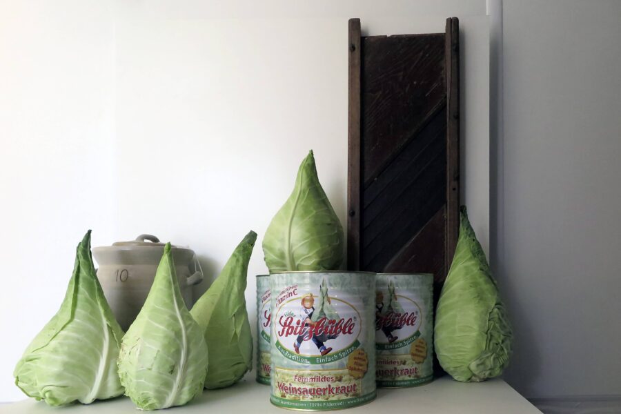 Spitzkohl, Sauerkrautdosen, ein Steinguttopf und ein Holzschneidebrett auf einem Tisch.