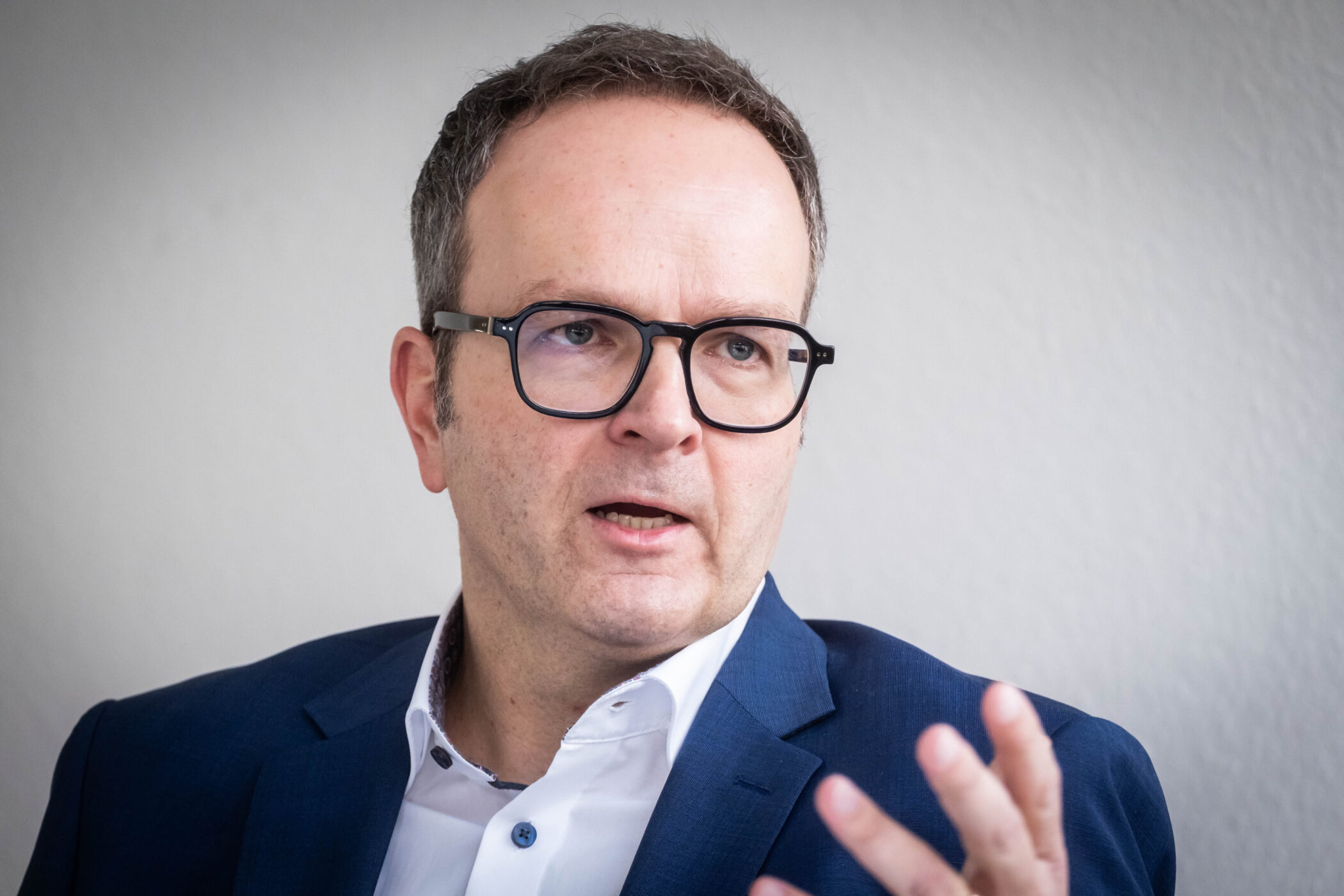 Mann mit Brille und Anzug spricht, Hand erhoben.