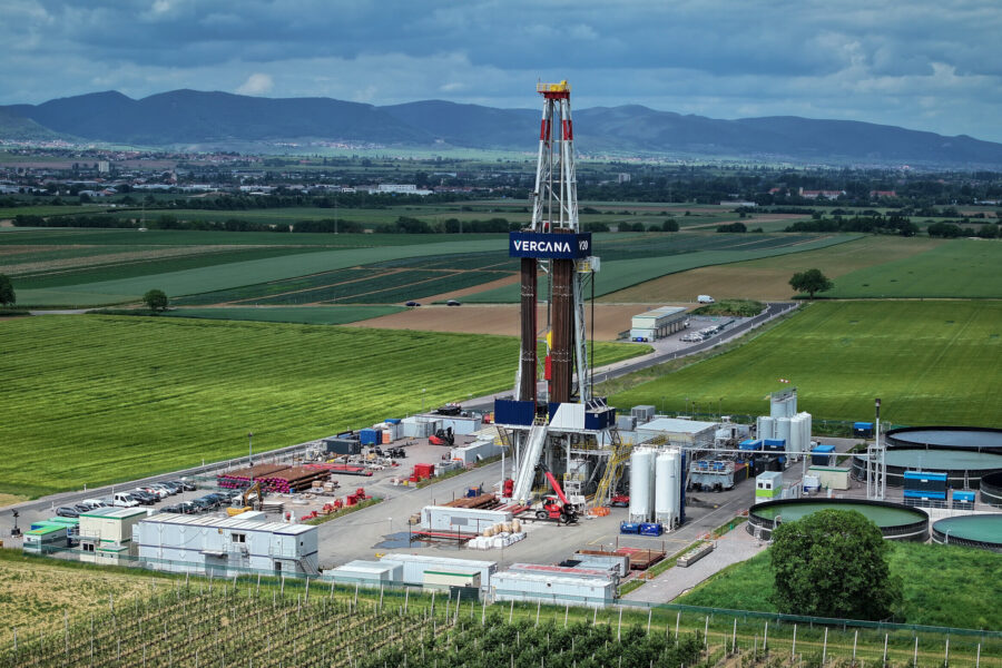 Bohrturm und Industrieanlagen auf einem Feld, Berge im Hintergrund.