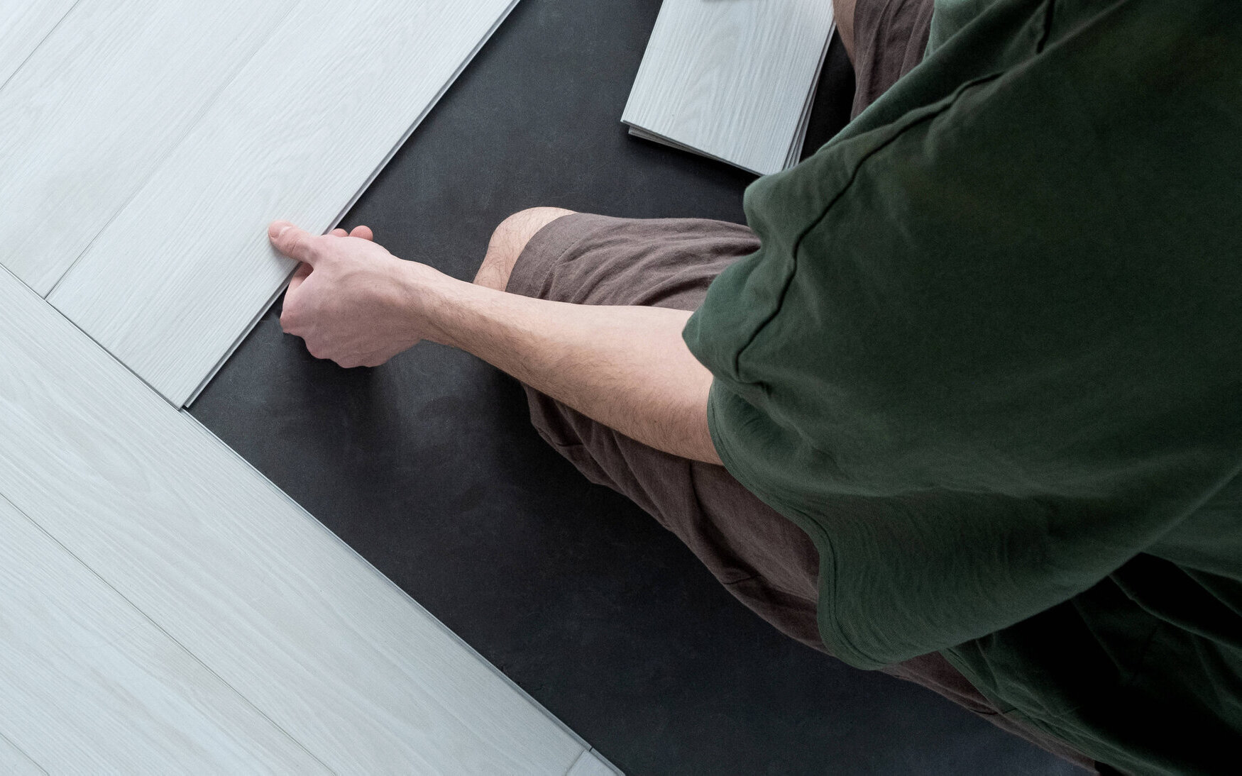 Person verlegt helle Laminatdielen auf dunklem Untergrund.