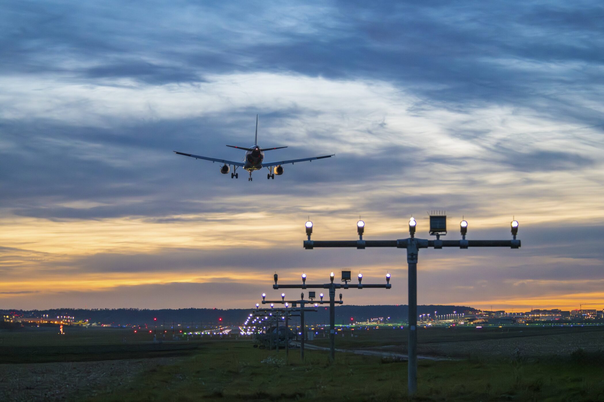 Flugzeug im Landeanflug bei Sonnenuntergang, Landebahnlichter im Vordergrund.