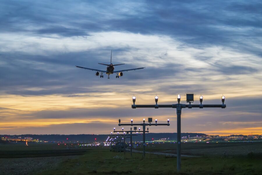 Flugzeug im Landeanflug bei Sonnenuntergang, Landebahnlichter im Vordergrund.