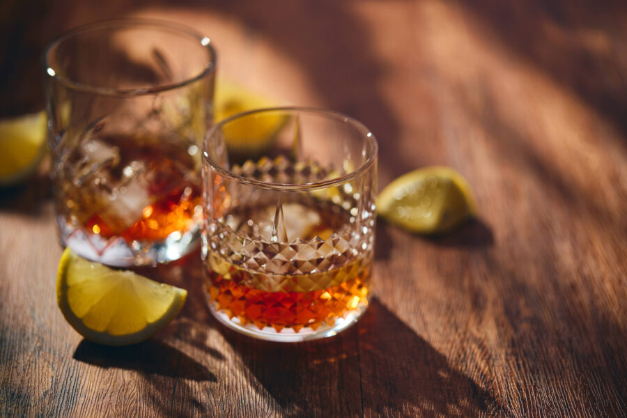 Zwei Gläser mit Getränk und Eiswürfeln, Zitronenscheiben auf Holztisch.