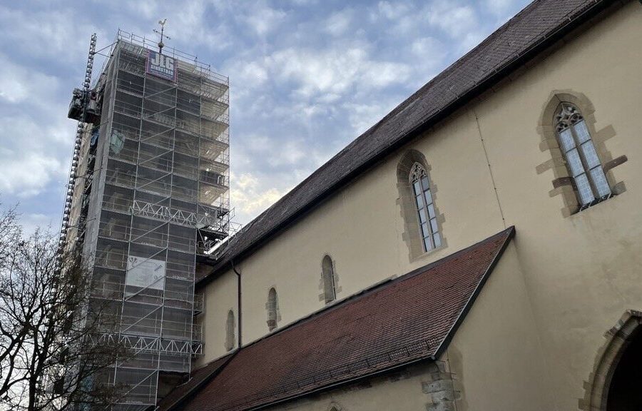 Kirchturm mit Gerüst, daneben Kirchengebäude mit Spitzbogenfenstern, bewölkter Himmel.