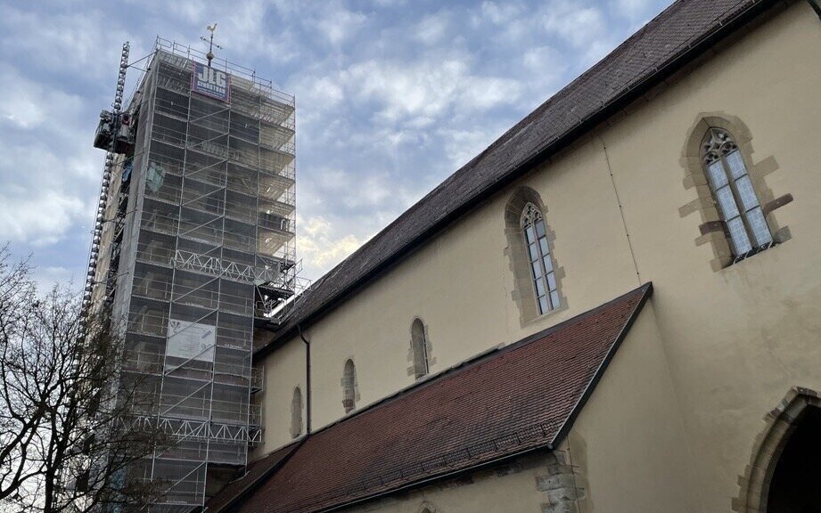 Kirchturm mit Gerüst, daneben Kirchengebäude mit Spitzbogenfenstern, bewölkter Himmel.