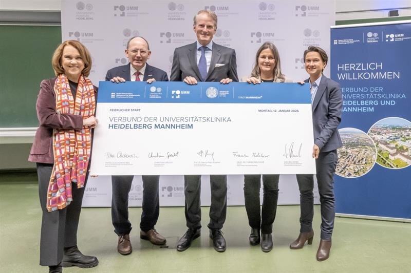 Fünf Personen halten ein großes Schild mit Text zu Universitätsklinika Heidelberg Mannheim.