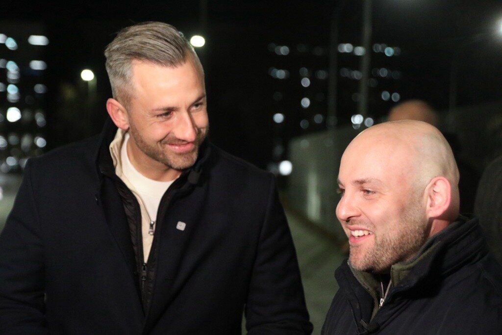 Zwei lächelnde Männer in Jacken bei Nacht.