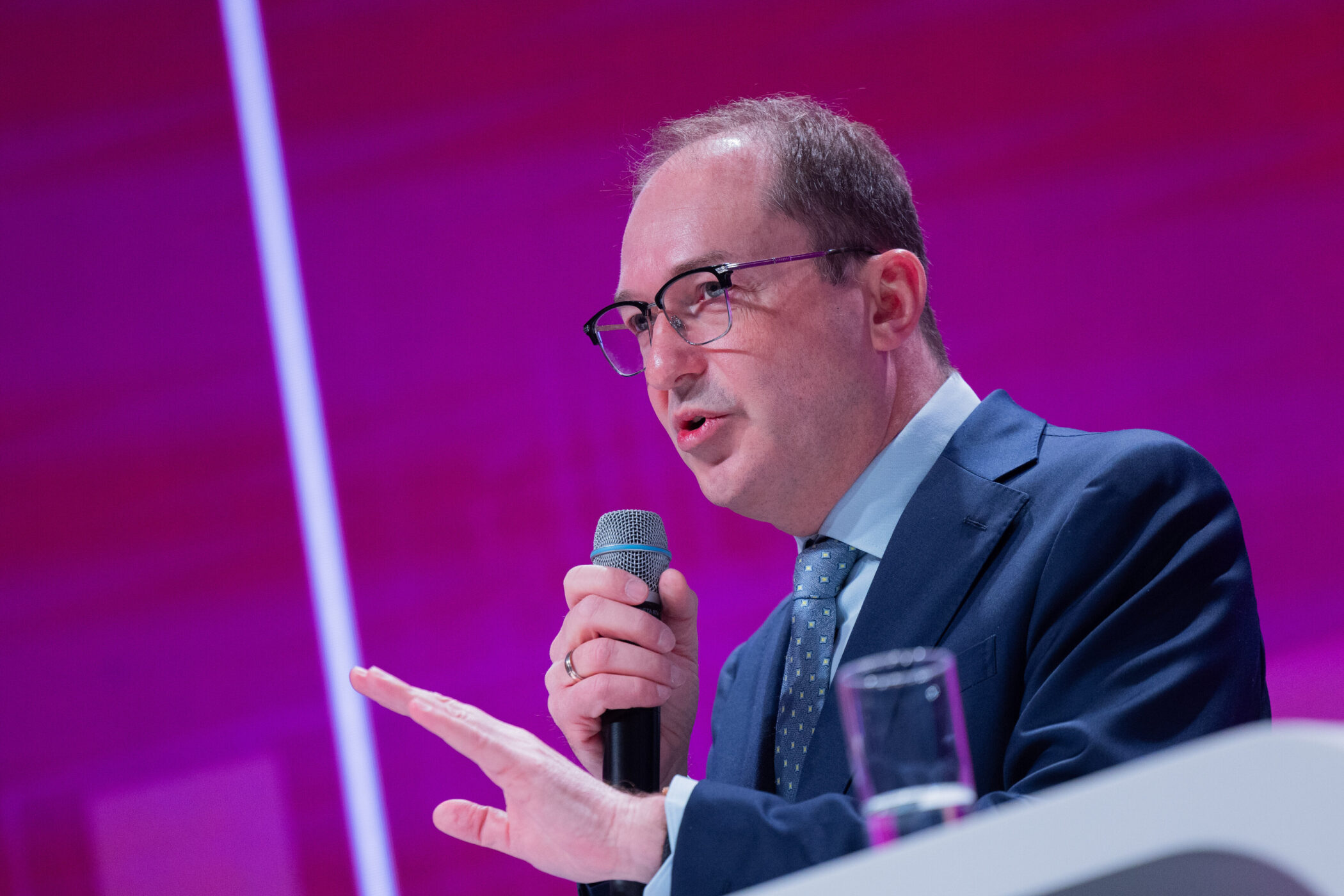 Mann mit Brille spricht in Mikrofon, Hintergrund lila.