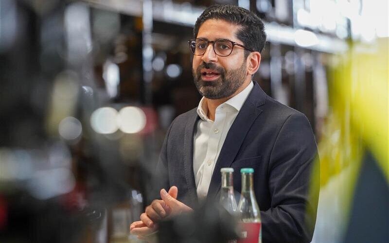 Ein Mann im Anzug spricht, vor ihm stehen zwei Flaschen.